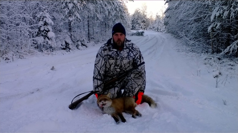 Metsästäjä kettusaalis kädessään talvessa